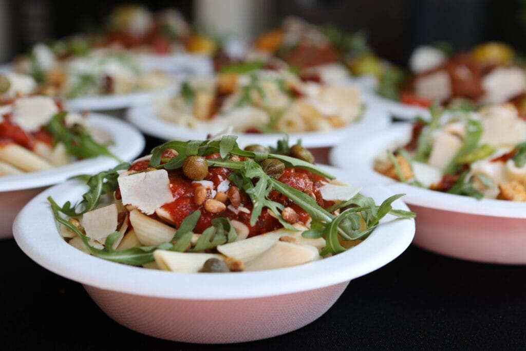 Witte schaaltjes met verse penne pasta, tomatensaus, rucola, pijnboompitten en Parmezaanse kaas van Capri Culinair.